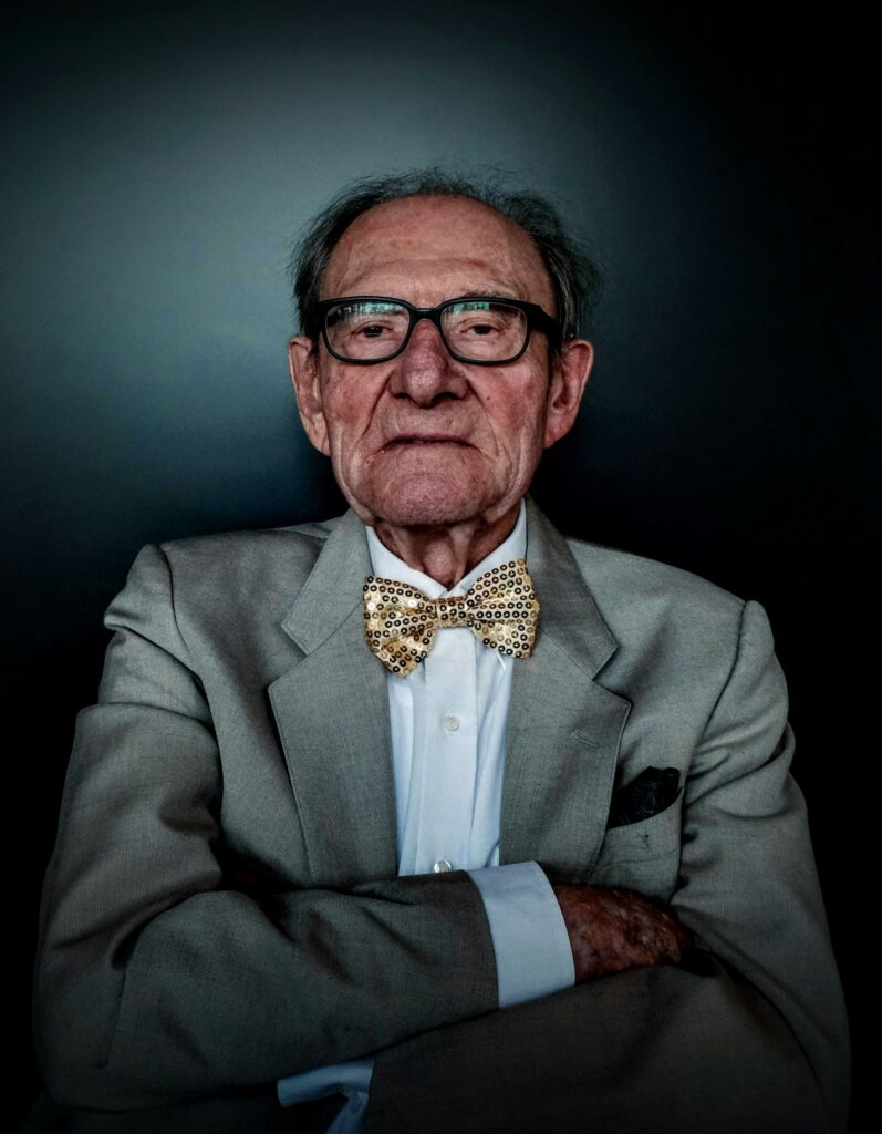 A distinguished senior business leader in a grey suit and bow tie