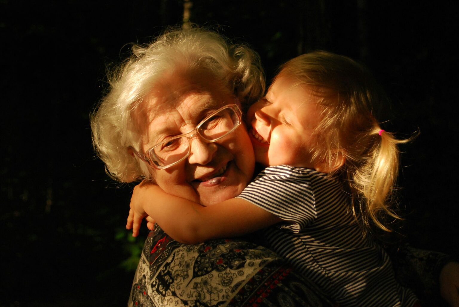A grandmother laughing as her granddaughter hugs her