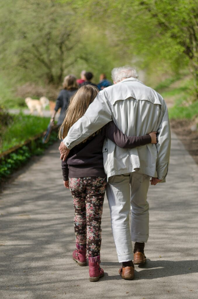 A grandfather and granddaughter walking arm in arm down a leafy path
